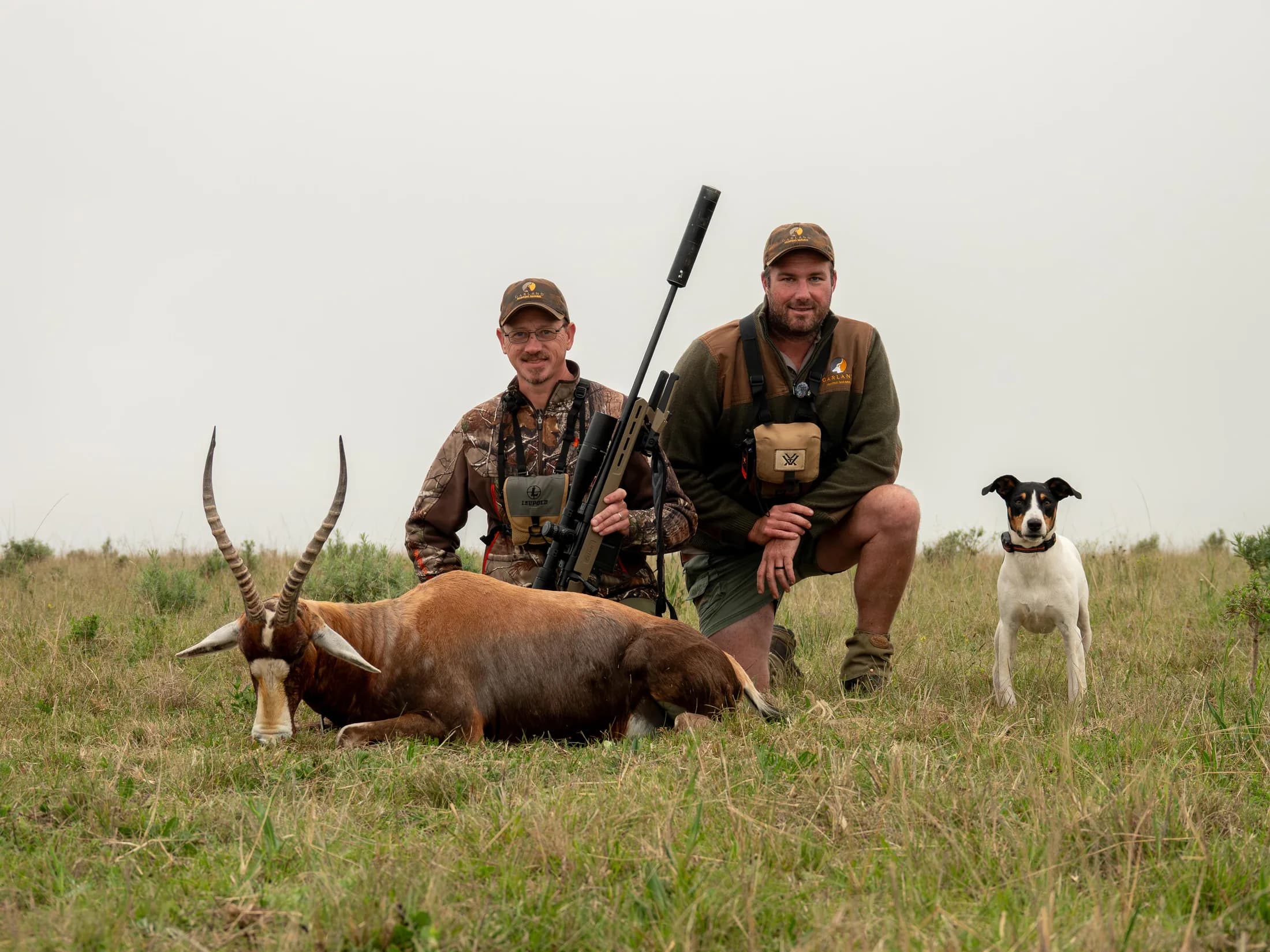Two hunters and a dog behind an antelope hunting trophy
