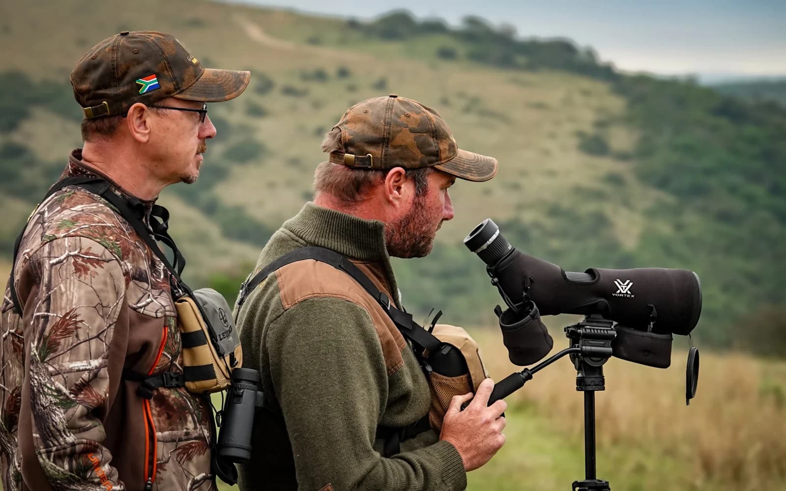 Two hunters observing the landscape through a spotting scope