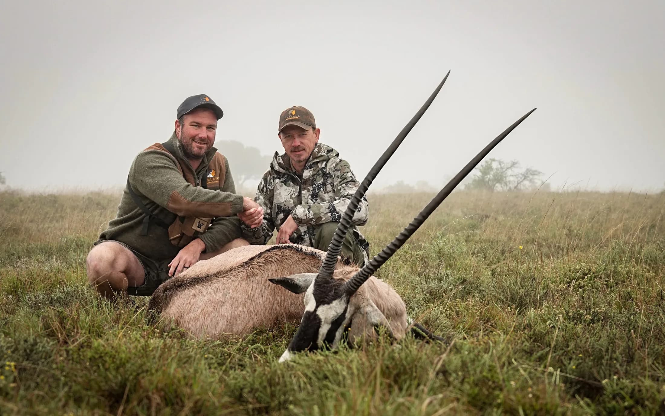 Two hunters behind a gemsbok hunting trophy in misty grassland