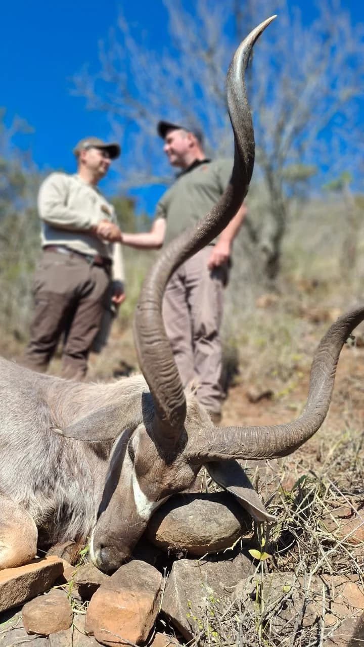 Two people shaking hands behind an antelope hunting trophy