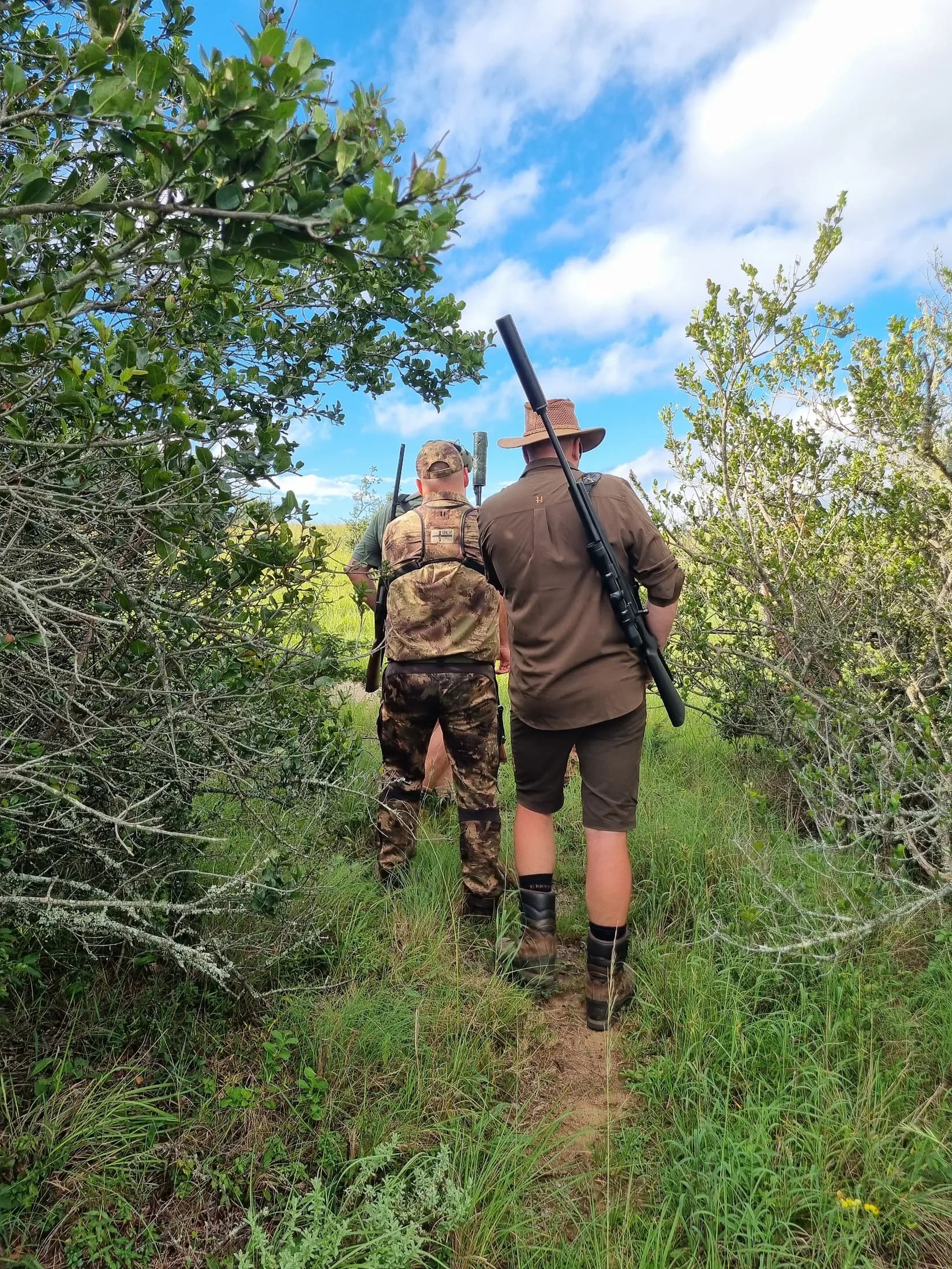 Two hunters carrying their equipment along a wooded trail