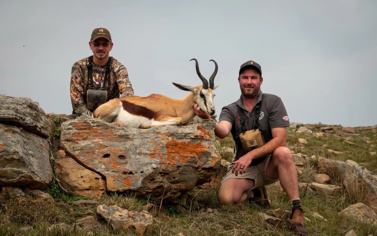 Two men with a harvested springbok on a rocky outcrop